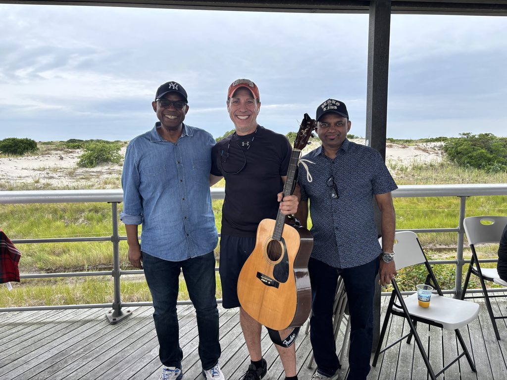 Alt text: Keith Rosen playing guitar with a morning prayer group on the Jones Beach boardwalk he connected with as a coach and human.